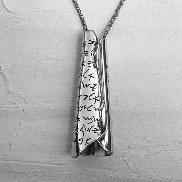 A large silver pendant in the shape of a scroll with an engraving in ancient Hebrew writing of the Priestly Blessing from the Book of Numbers